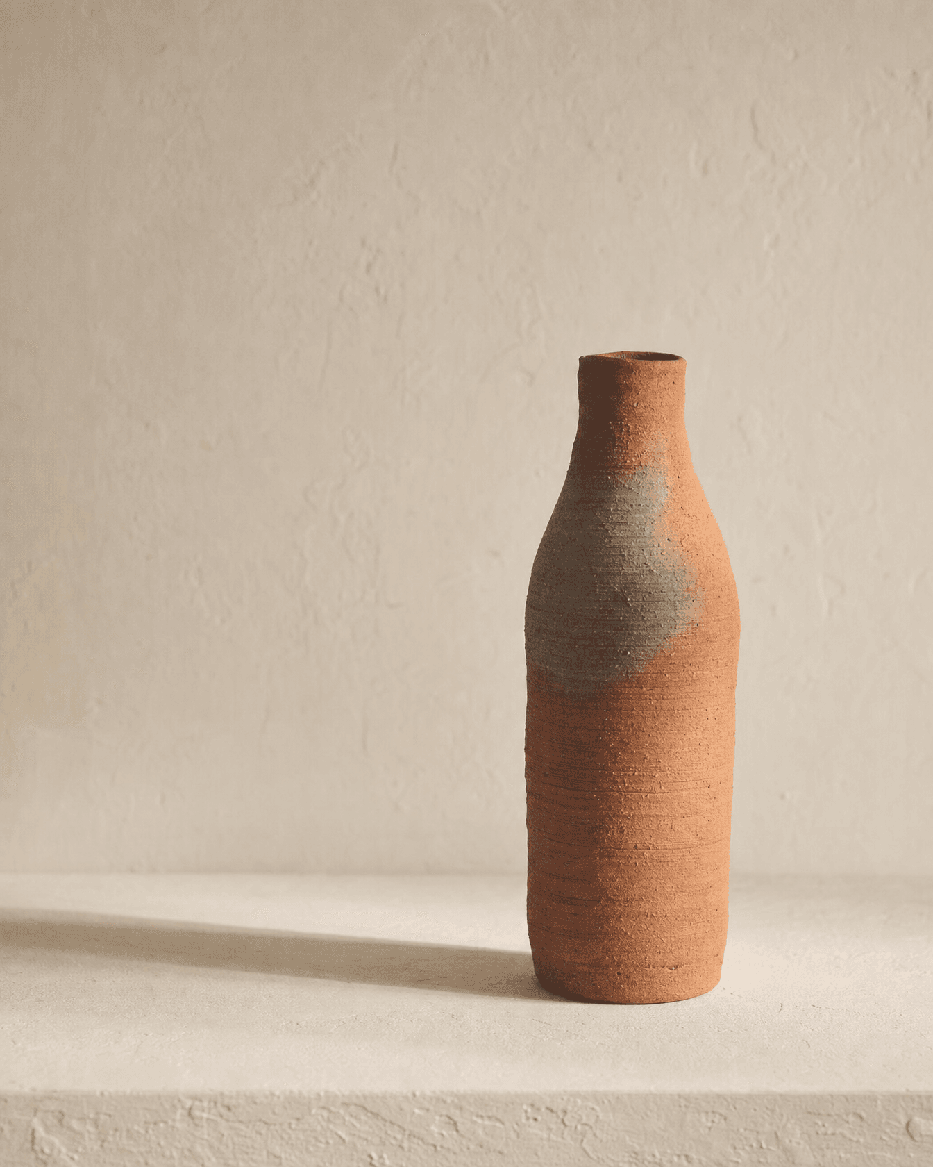 Tall hand-coiled terracotta bottle with ash-grey fire flashing